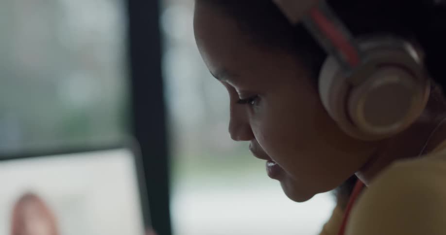 A girl sits at home wearing headphones and talking with a woman on her laptop