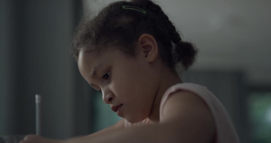 A young girl sitting indoors concentrates on what she is writing