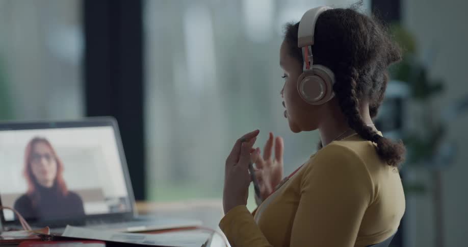 Brunette girl with headphones and braids makes video call with woman with red hair and black pullover on laptop