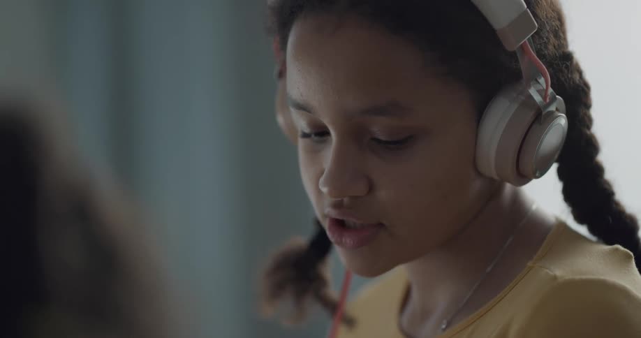 Brunette girl with braids and yellow shirt wears headphones and talks to person