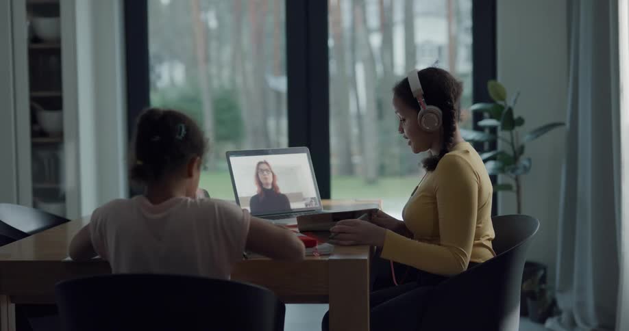 Two young girls taking online classes on a laptop at home