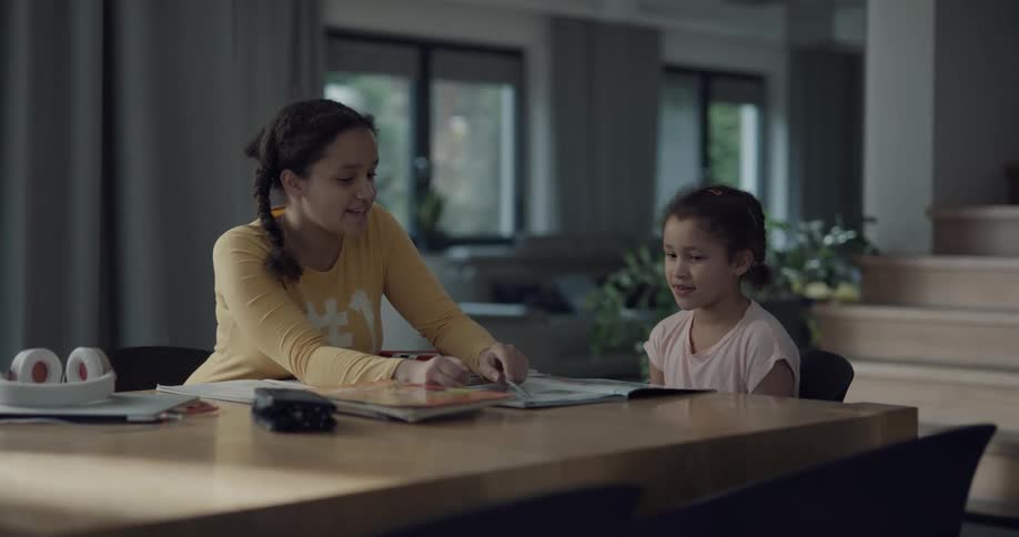 A young woman points at a book with a pencil while a young girl reads out loud