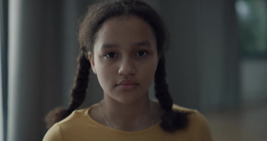 Young girl with pigtails looking at the camera while standing inside a room at home