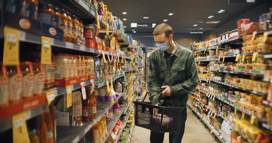 A young caucasian man in a plaid green shirt shopping at the grocery store