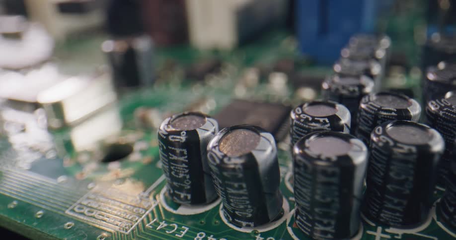 Close up of a green circuit board with black and metal components and white letters and numbers