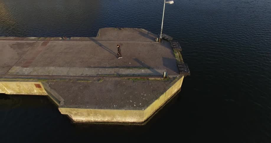 A woman standing on the end of a pier turns around and jogs the other direction