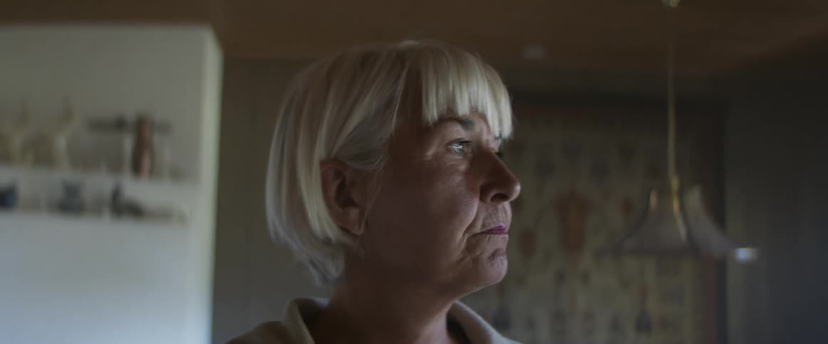 Side view of a middle aged woman with grey hair looking out the windows in living room