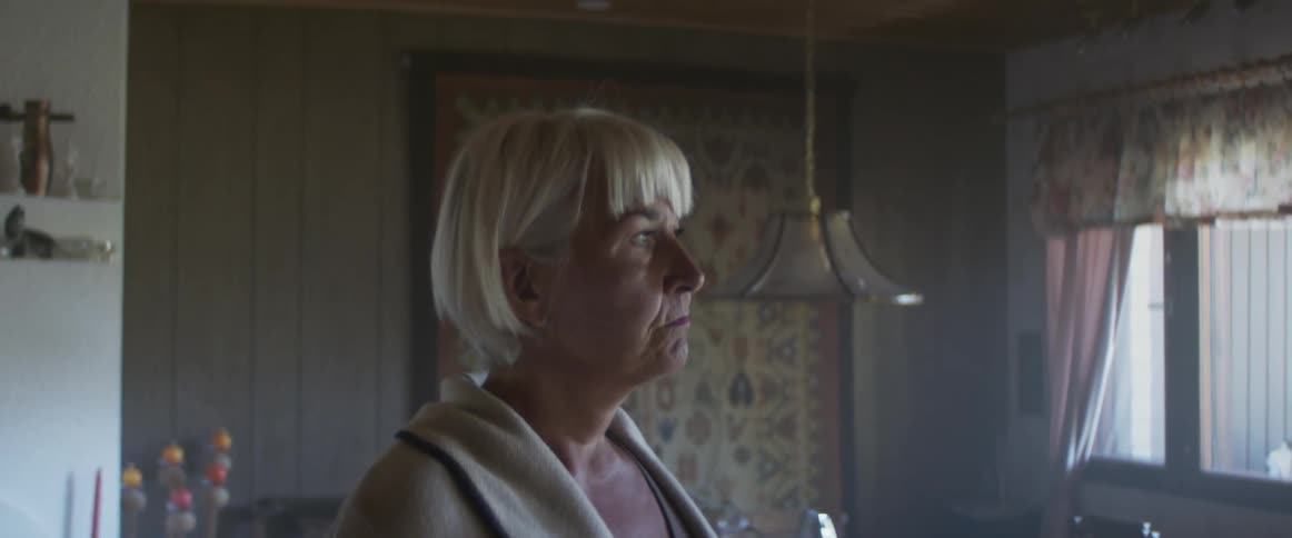 Blonde middle aged woman walks and looks out the windowsin the living room