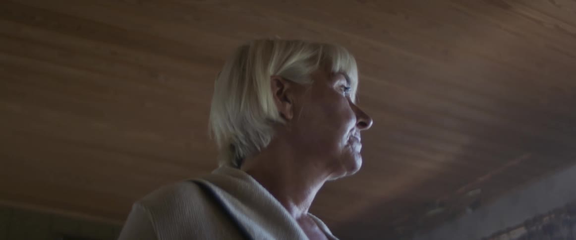 A middle aged woman stands in a room in a house and gazes towards the window