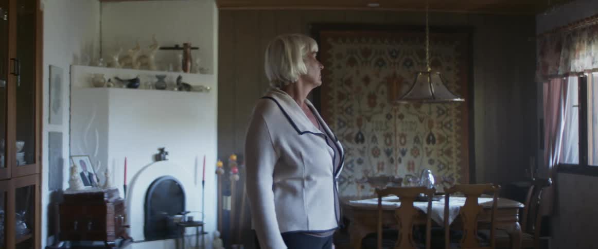 A woman walks from a room into the living room and stops to look out the window