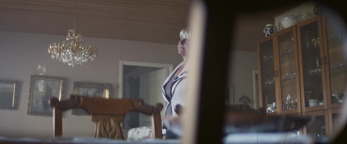 Senior woman stands pensively in the middle of the dimly lit living room at home