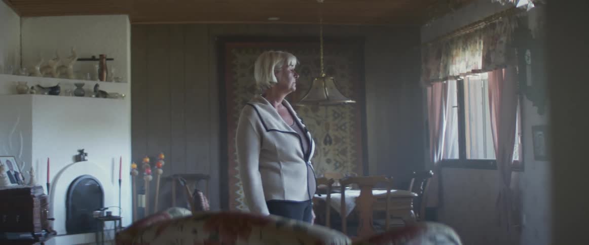 A woman at home looks out the window and wipes a tear away