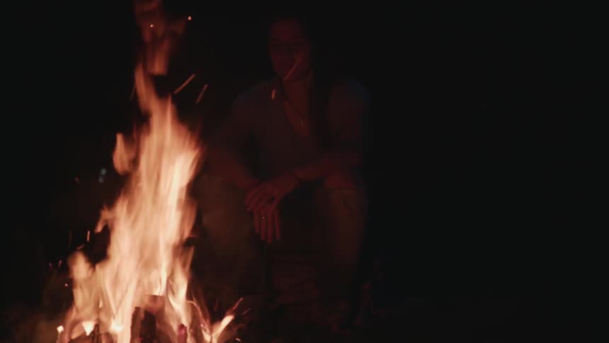 A woman sits in front of a burning fire