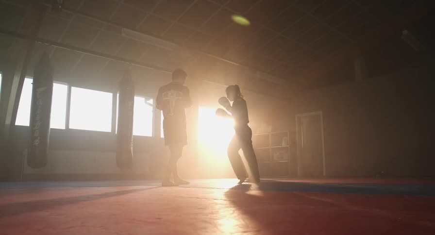Woman practicing kickboxing while man holds protective padding