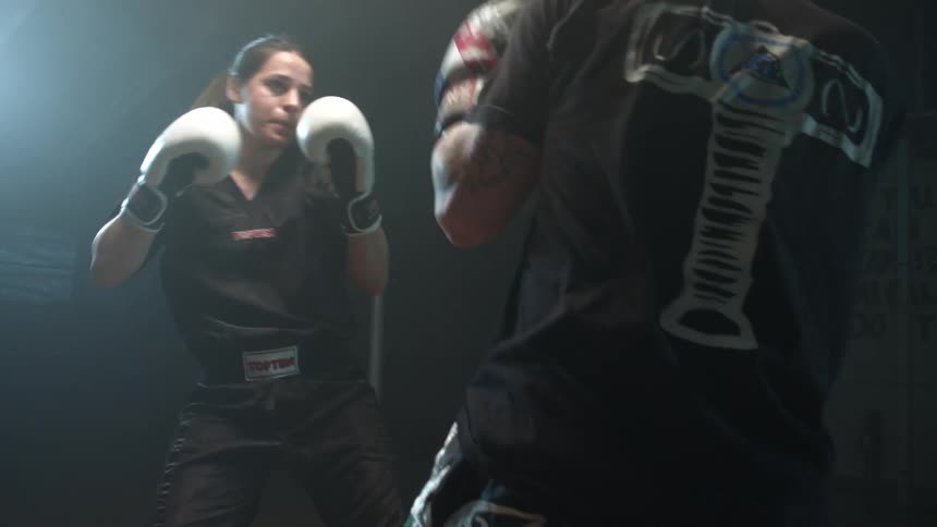 A man and a woman spar with each other in a boxing gym