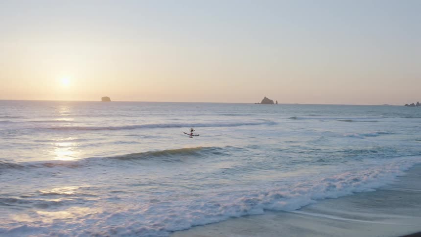 Air to air traverse of a drone flying over crashing waves along the coast at sunset