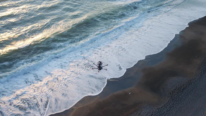 Tilt down follow of a hexacopter drone flying along an ocean shoreline