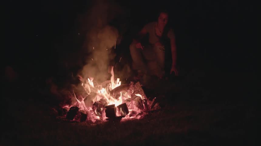 A woman feeds a campfire