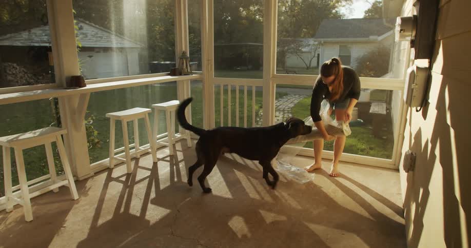 A woman on her porch with her dog is unwrapping plastic from a rolled up rug