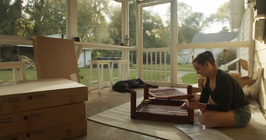 A woman assembling a wooden coffee table on the floor of a sun room