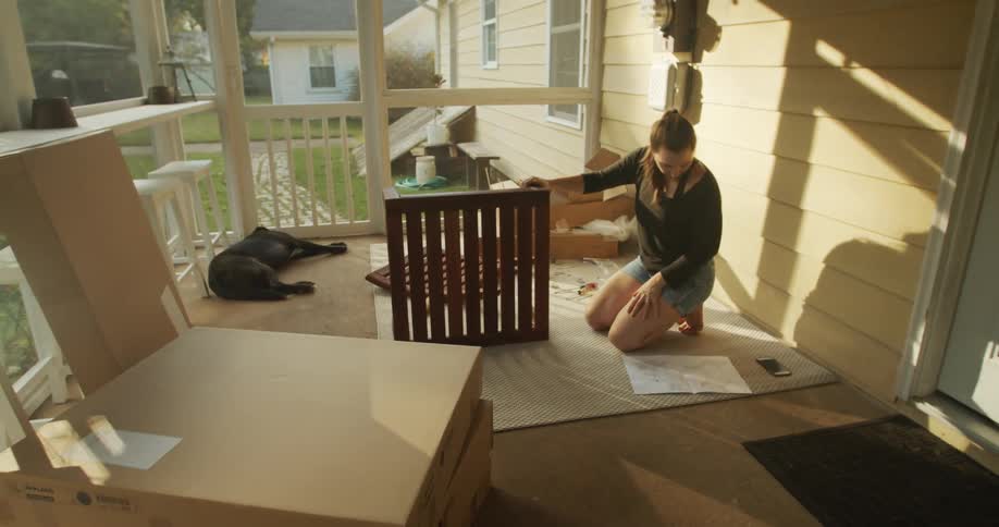 A woman looks at the instructions as she puts wooden furniture together on her screen porch