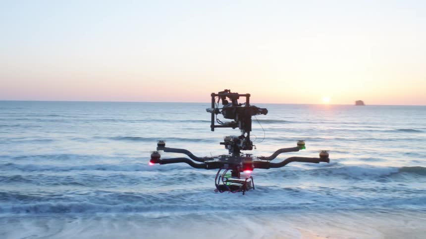 Aerial orbit around a large drone flying over a beach at sunset