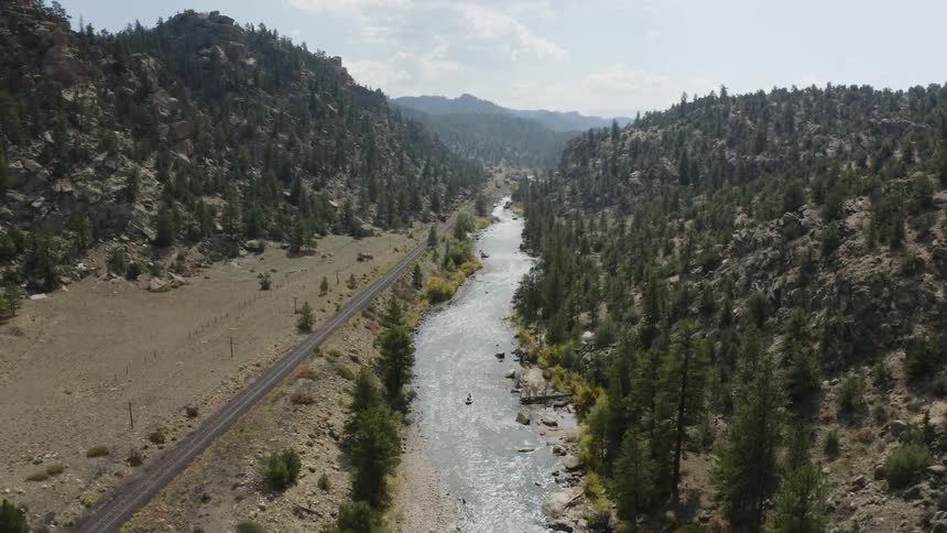 River valley with tall pine trees along the mountainous terrain and mountains on the horizon on a cloudy day