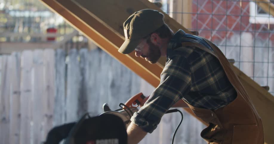 A carpenter prepares to cut a piece of wood with an electric saw outside the house at sunset