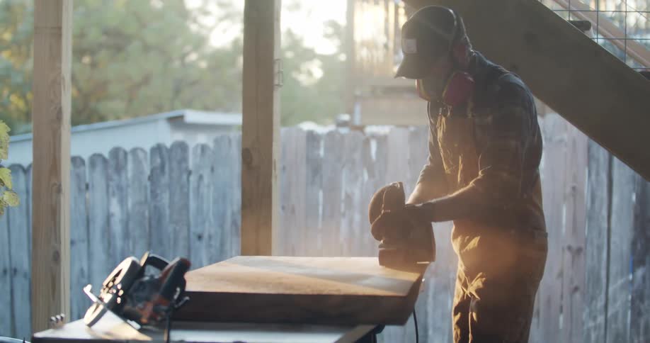 Worker sanding a plywood board over a table outside a house at sunset
