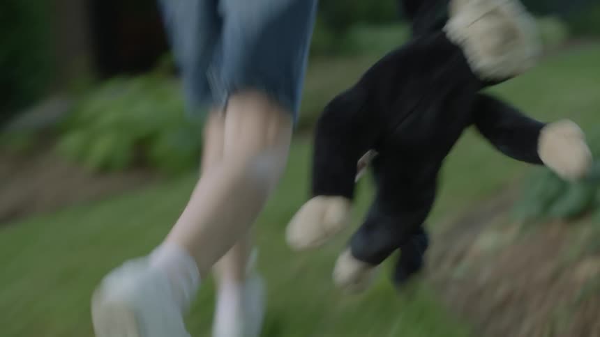 Child wearing denim shorts carries a stuffed animal while running on the lawn next to a car