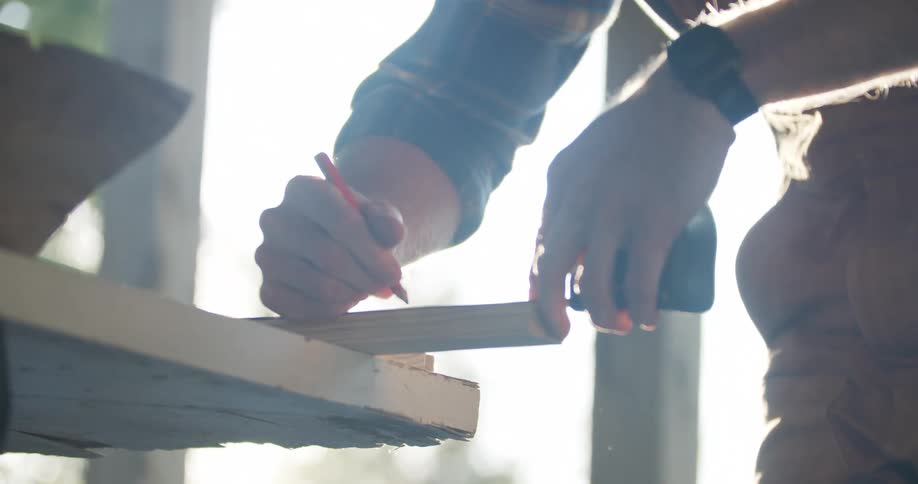 A construction worker measuring a piece of wood with a tape measure and pencil
