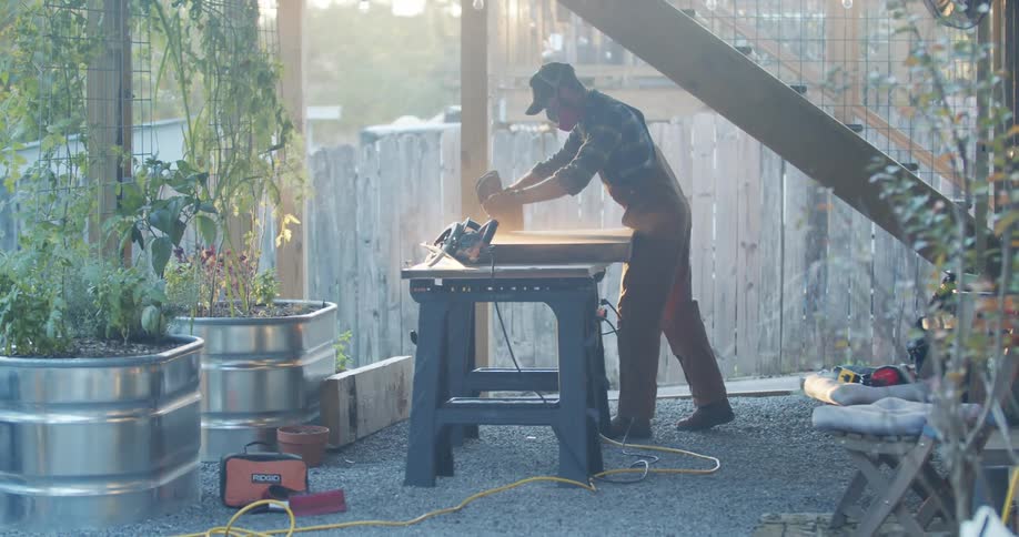 Carpenter sanding a pierce of wood over a workbench outdoors at sunset