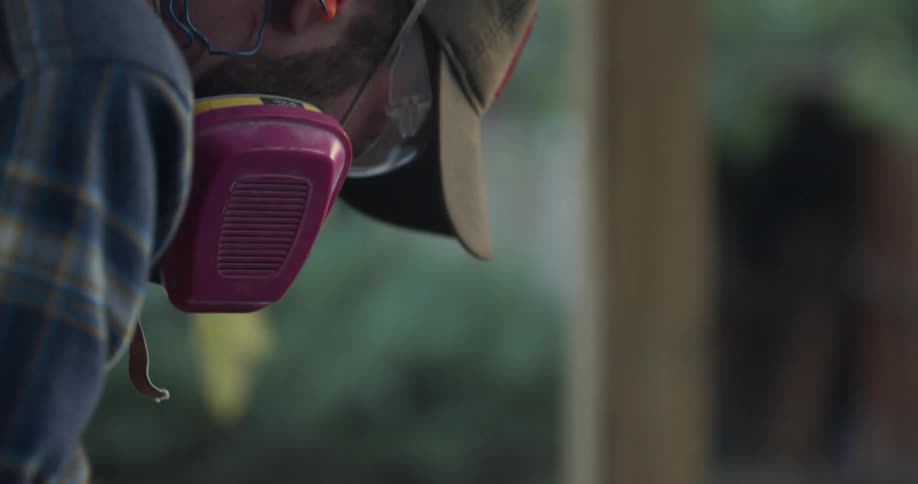 A man wears safety glasses and a gas mask while cutting on a porch outdoors