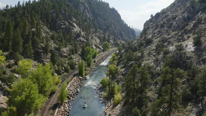 A person paddles down a river surrounded by mountains on a clear day