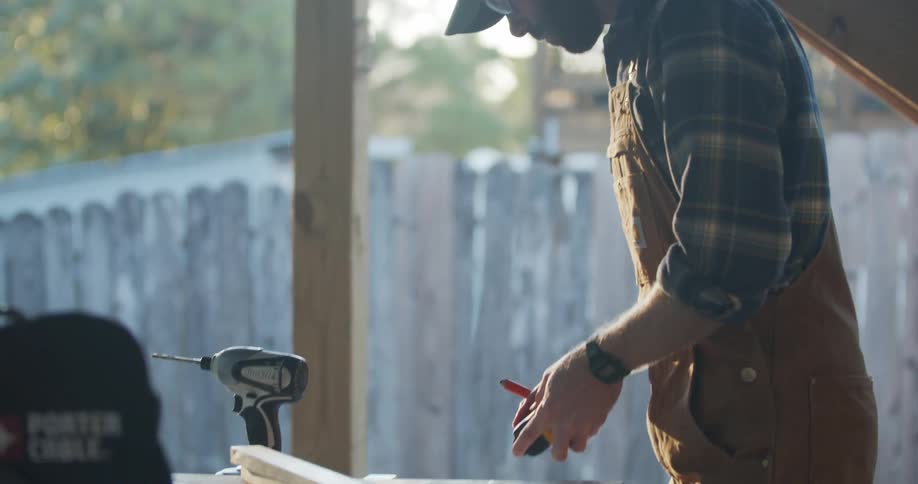 A carpenter in a back yard measures wood