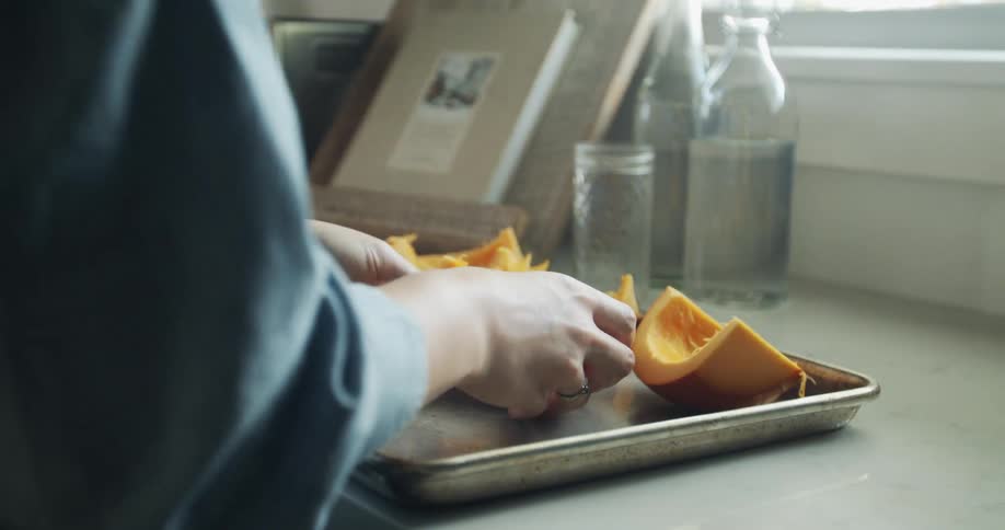 A woman places food on a baking sheet in a kitchen