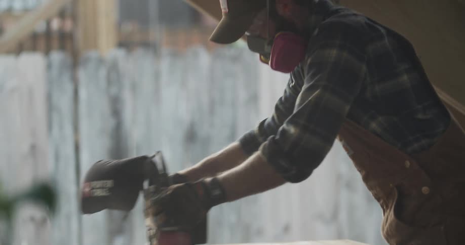 Carpenter sanding the surface of a board over a table outside home at sunset