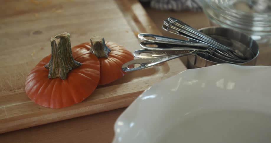 A kitchen counter with a cutting board pumpkin stems measuring cups and white and glass bowls