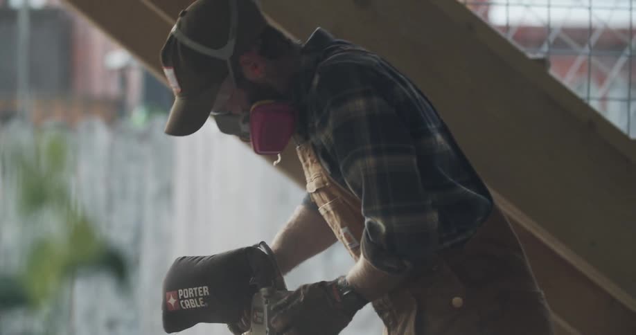 A man sanding a wooden board over a table outside a house at sunset