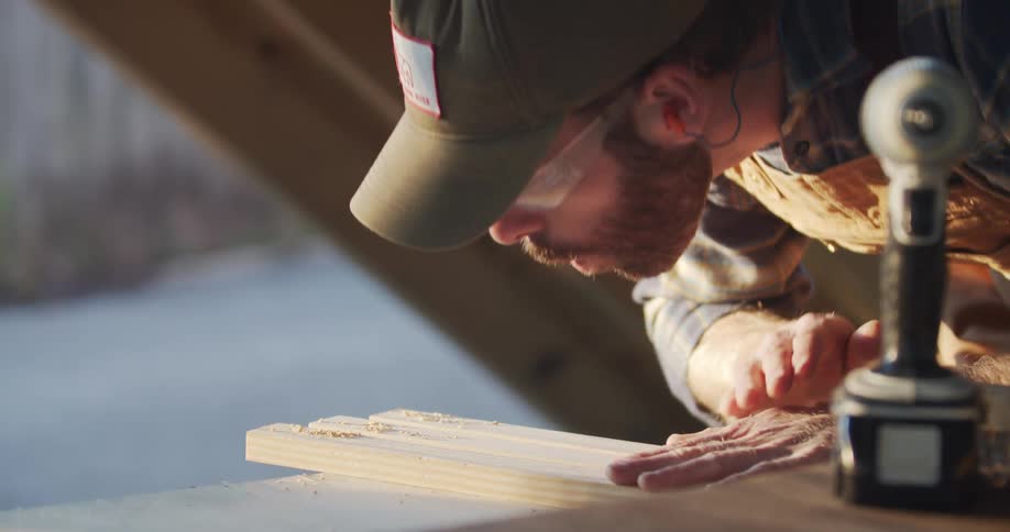 A construction worker uses a power drill and blows the dust off of the board