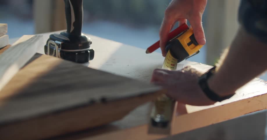 A man uses a measuring tape to measure a piece of wood