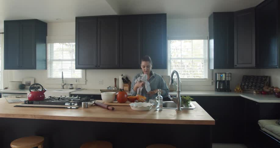 A woman cooking in her kitchen wipes her hands on a towel