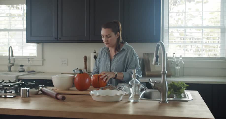 A woman cuts a pumpkin while standing at a counter in her kitchen