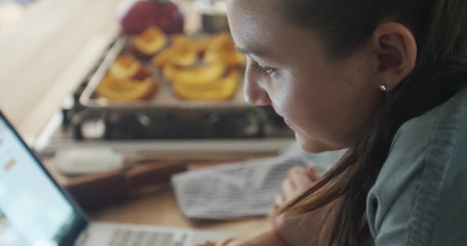 A woman looks at a laptop on her kitchen counter