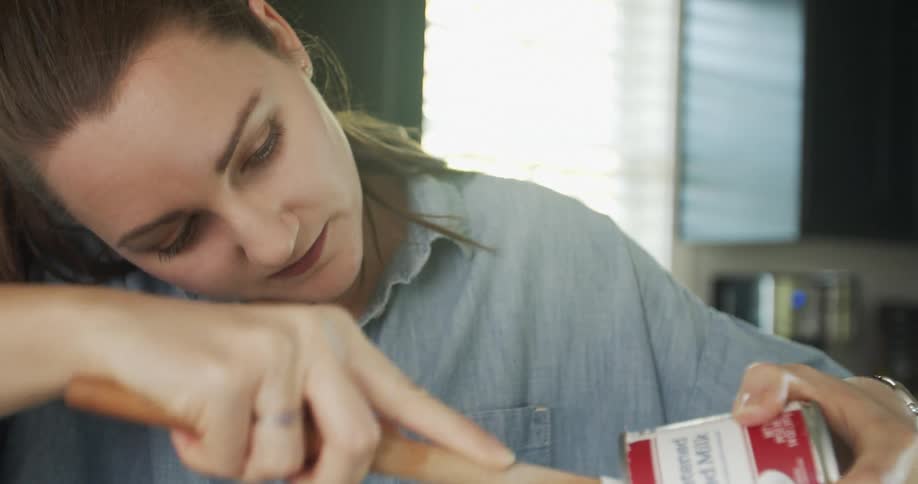 A woman in a room with a utensil removing frosting from a can