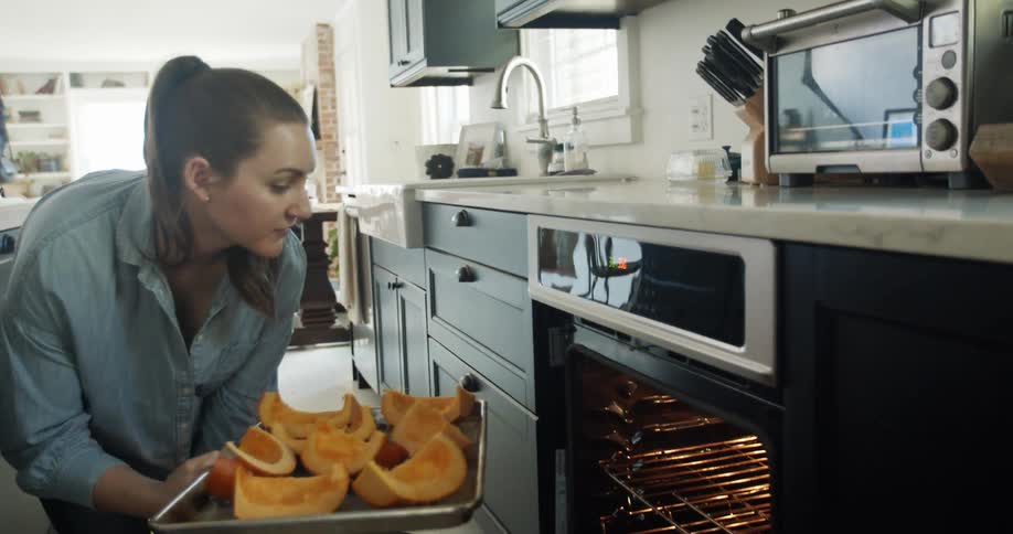 A woman putting a tray of sliced pumpkins in the oven to bake