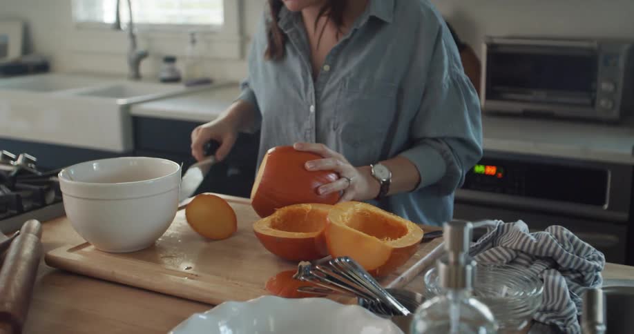 A woman cuts a pumpkin on a cutting board in a kitchen