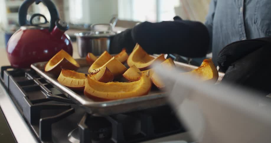 Woman using oven gloves places a tray with cooked pumpkin slices over the kitchen