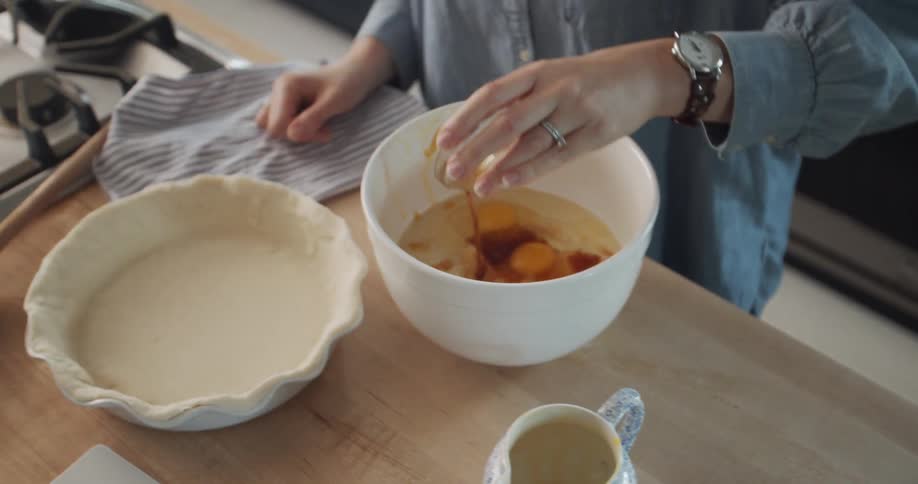 Woman pours ingredients from small bowl on table to large bowl with eggs