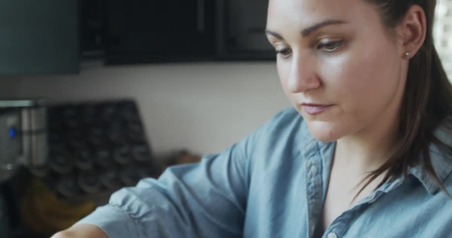 A woman stands in a kitchen using a knife on food